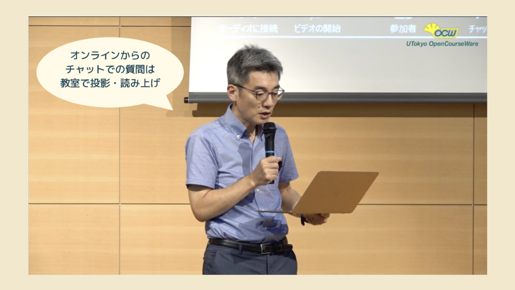 教室で、ノートパソコンを片手に、オンライン参加者からチャットで届いた質問を読み上げている石井先生の写真